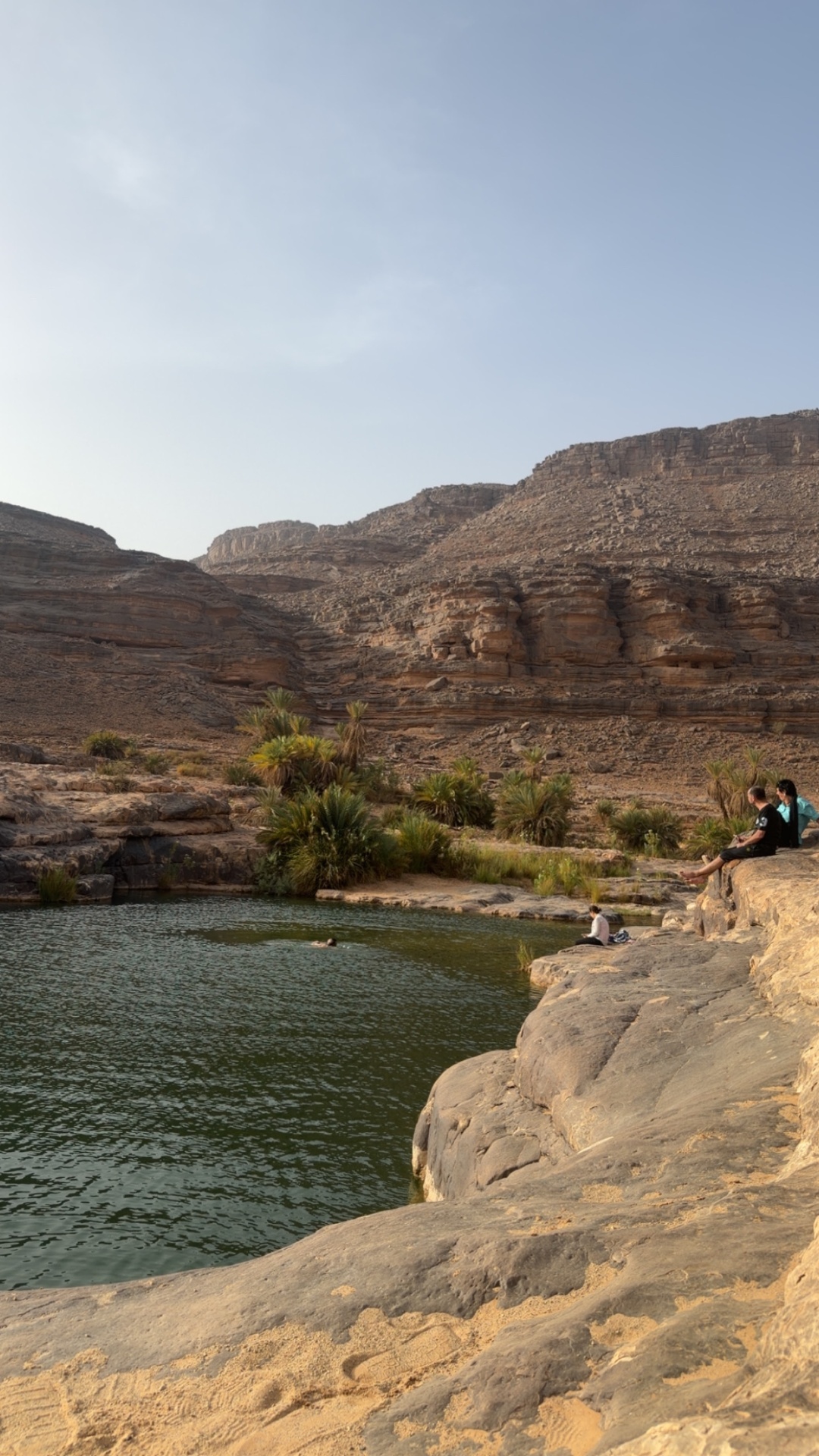 Voyageurs assis au bord d’une guelta face aux falaises